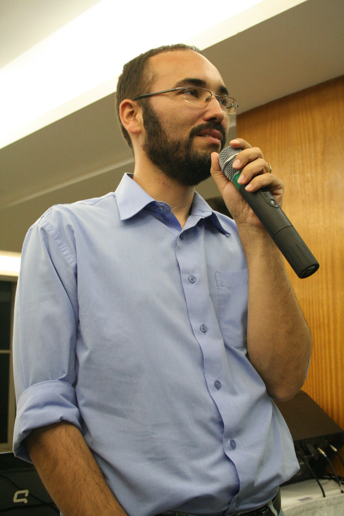 man wearing glasses holding a microphone looking away