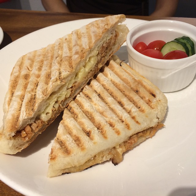 a grilled sandwich next to a small bowl of fresh vegetables