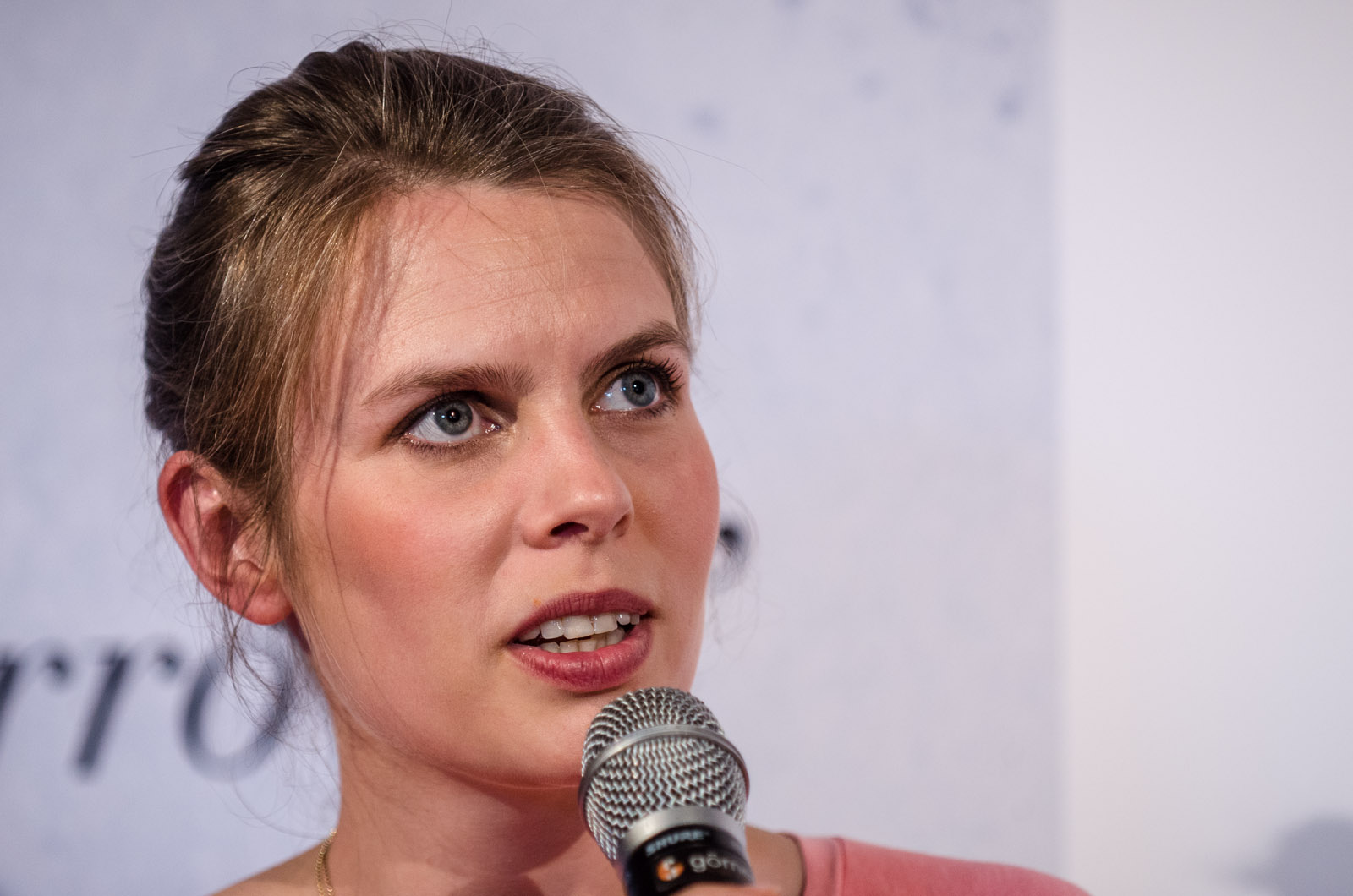 a woman in a pink top and black necklace is giving a speech