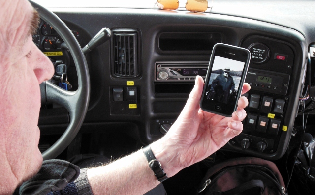 a person sitting down with their phone showing an image of himself on a car dashboard