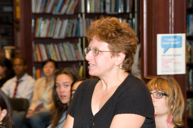 many people gathered together in front of a shelf with many books