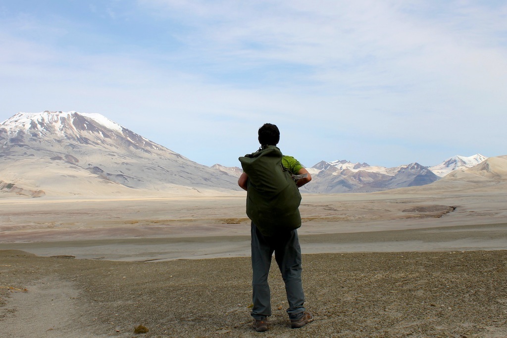 man with green coat watching mountains from sand