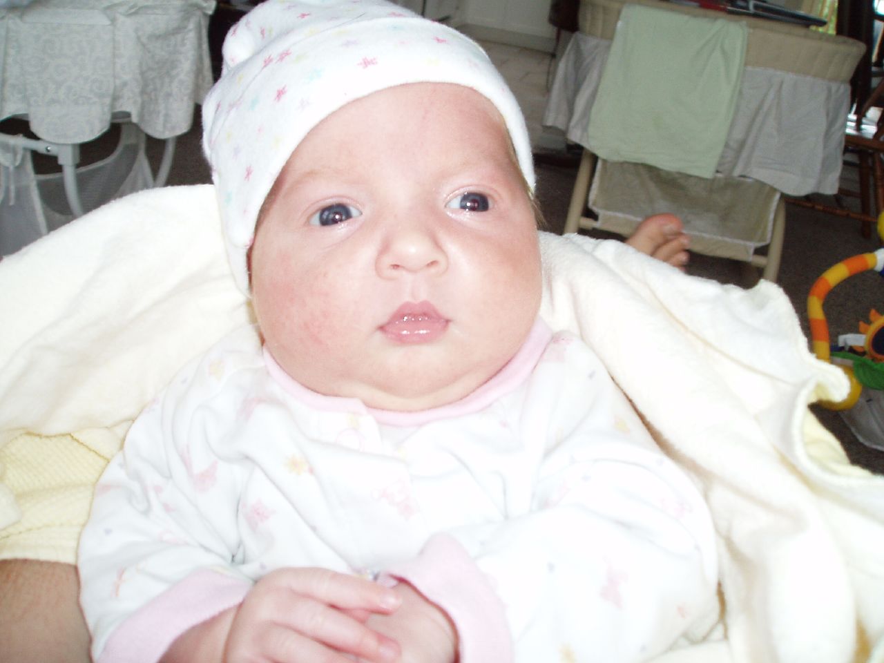 a baby in pajamas and a hat sitting under covers