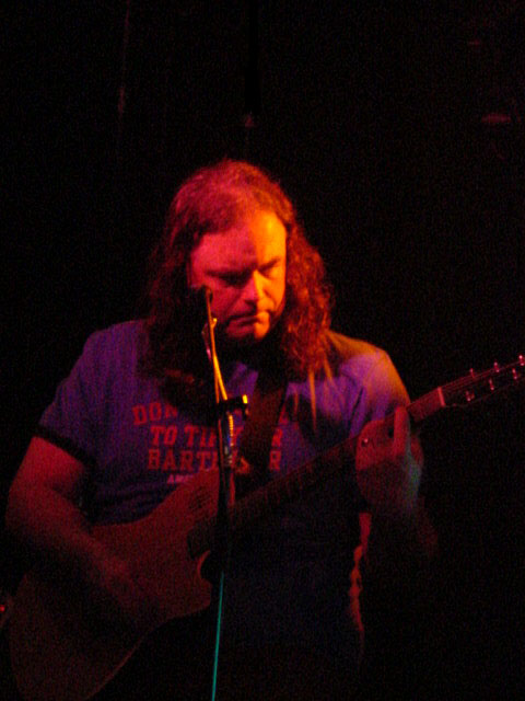 a man in blue shirt playing a guitar on stage
