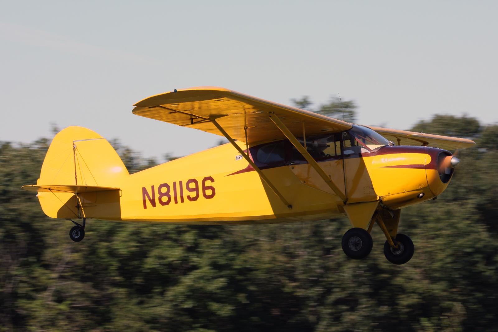 a yellow propellor airplane landing in front of trees