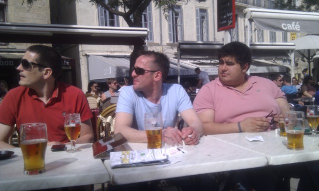 three men are sitting at a table with beer and pizza