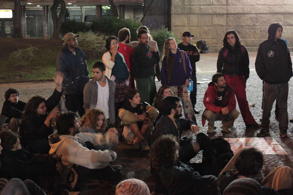 a group of people stand next to each other, with one sitting in the middle of the floor and many standing around them