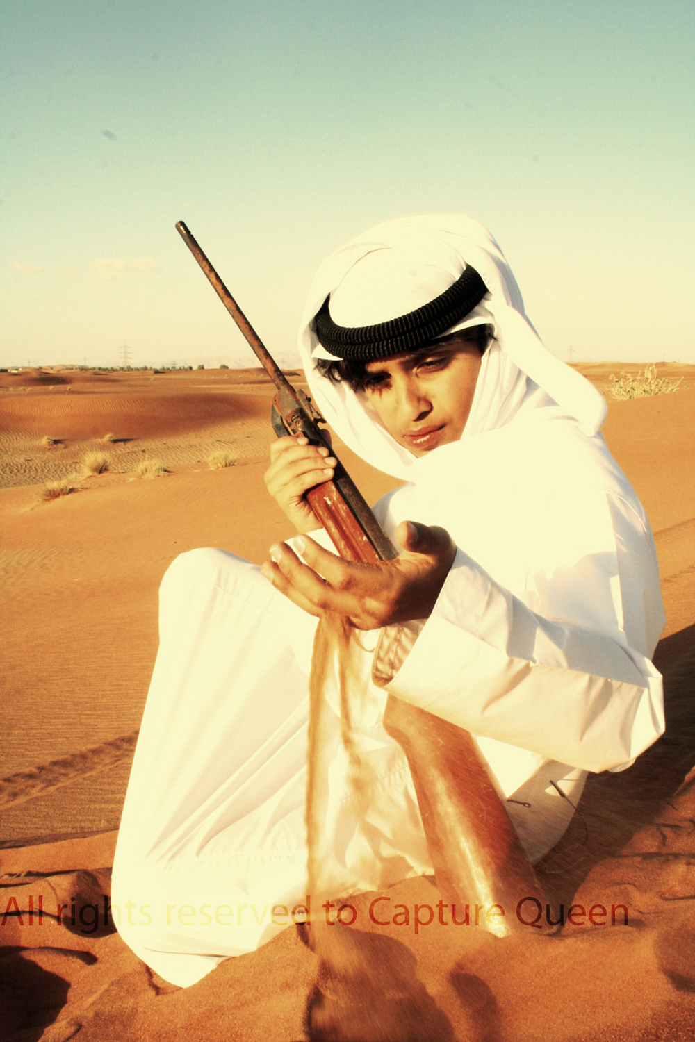 a man is holding a rifle and kneeling in the desert