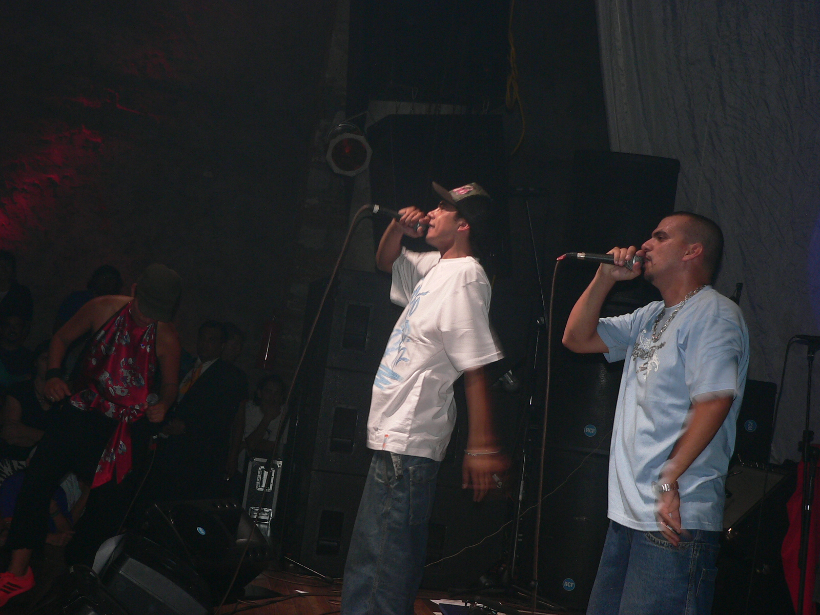 two men on stage with microphones and band watching