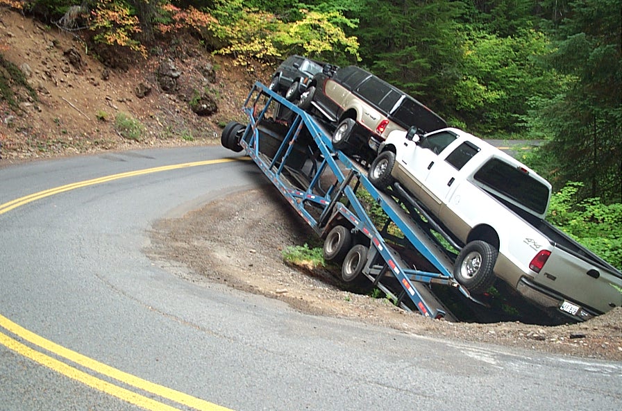 a truck carrying another vehicle on a hill side