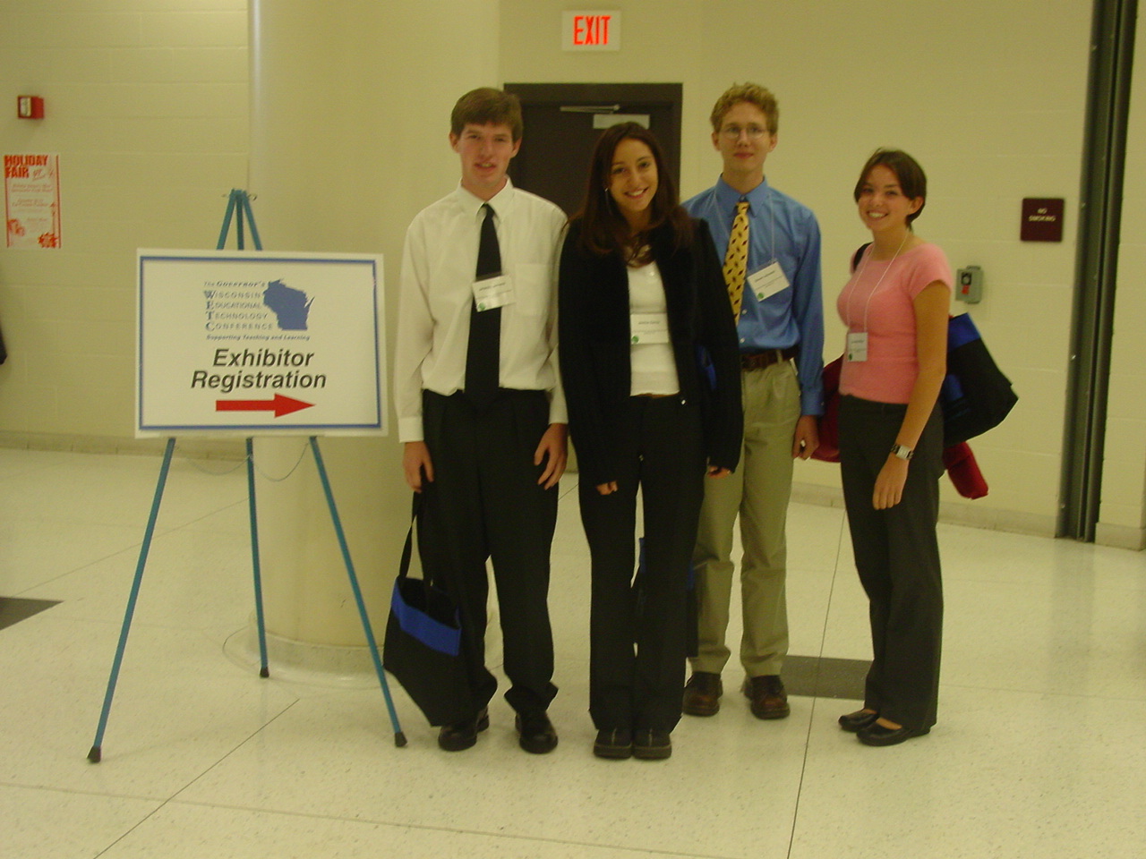 five smiling people posing in a hall in front of a sign