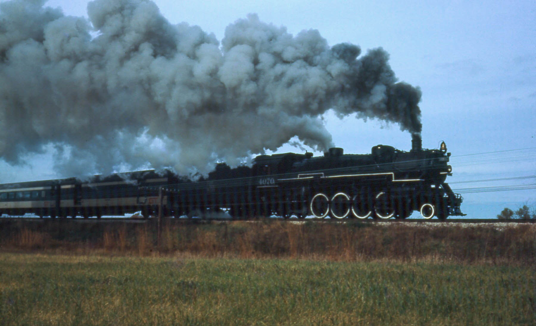 steam rises from the top of a train passing by a grassy field