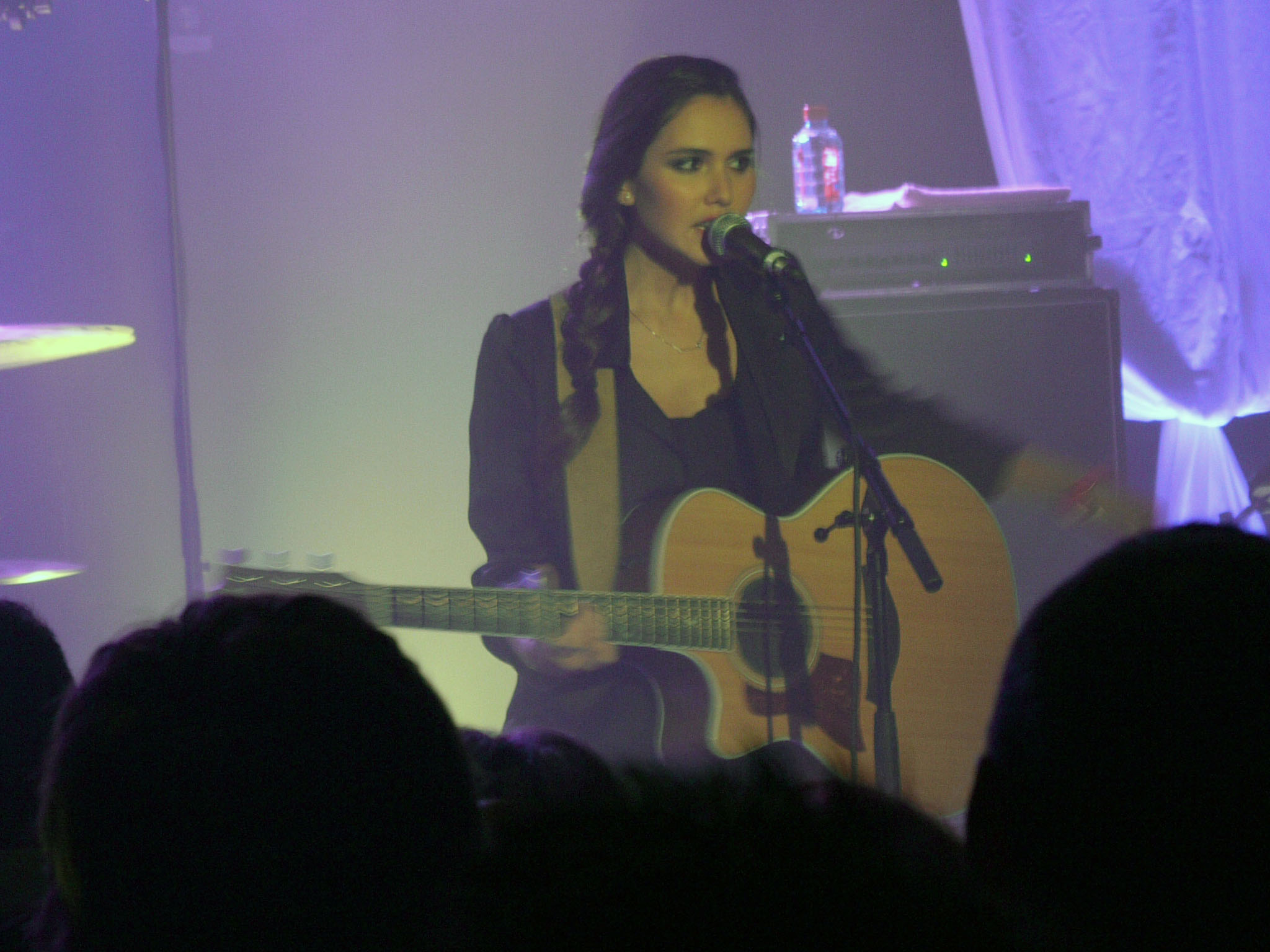 a woman holding a guitar singing in front of people