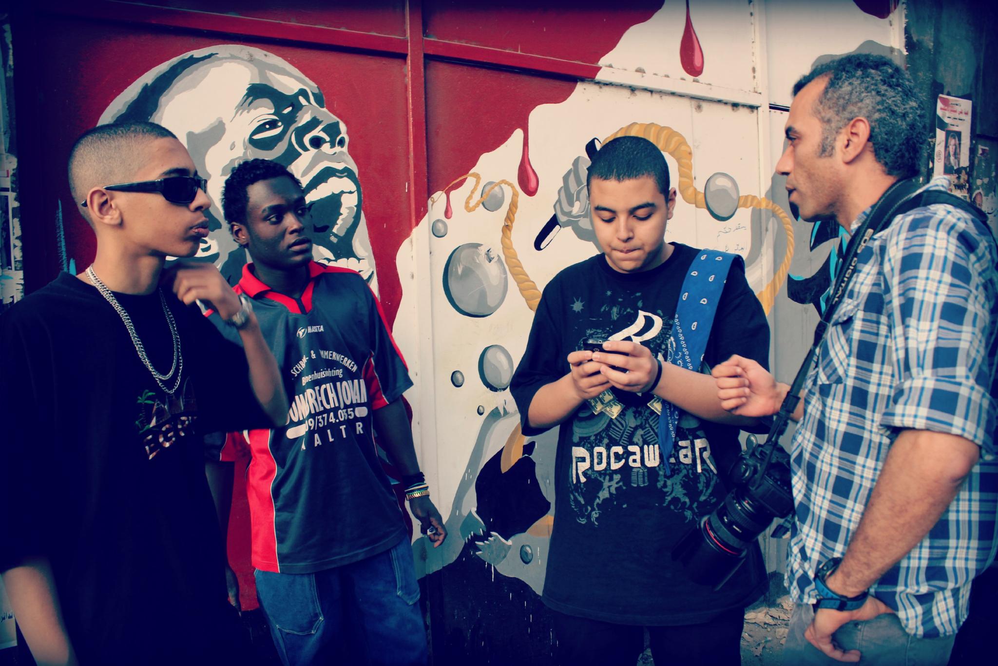 a group of young men standing around looking at a cellphone