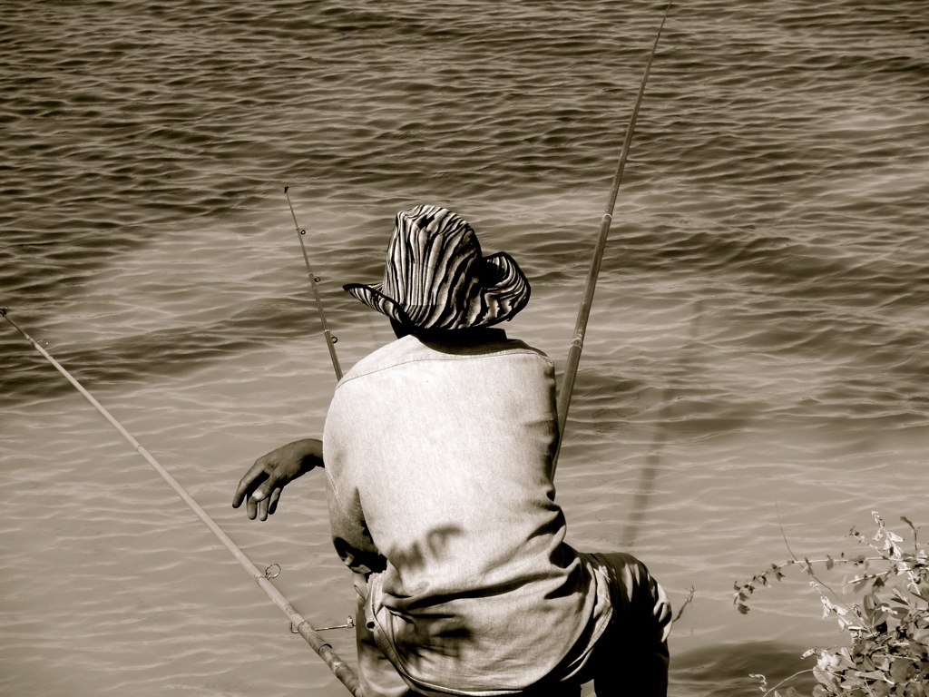 a person sits on the shore line with his fishing pole