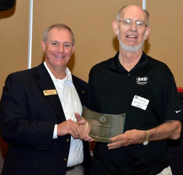 two men smile as they hold an award