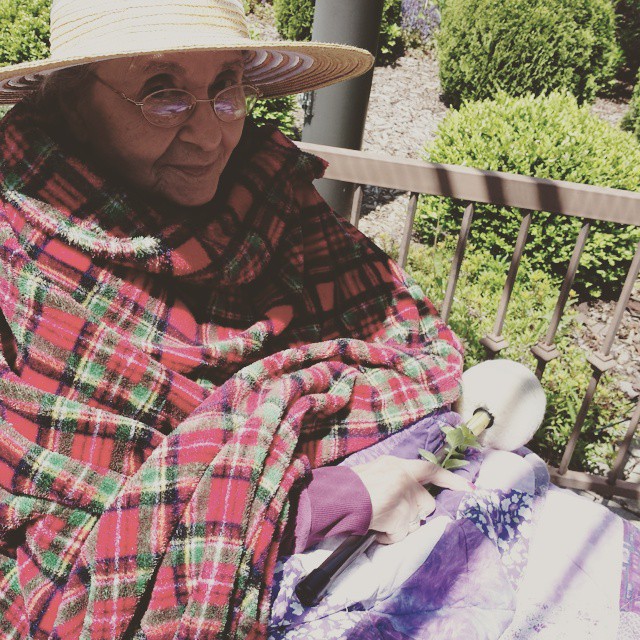 an older lady sitting on a bench with a blanket over her shoulder