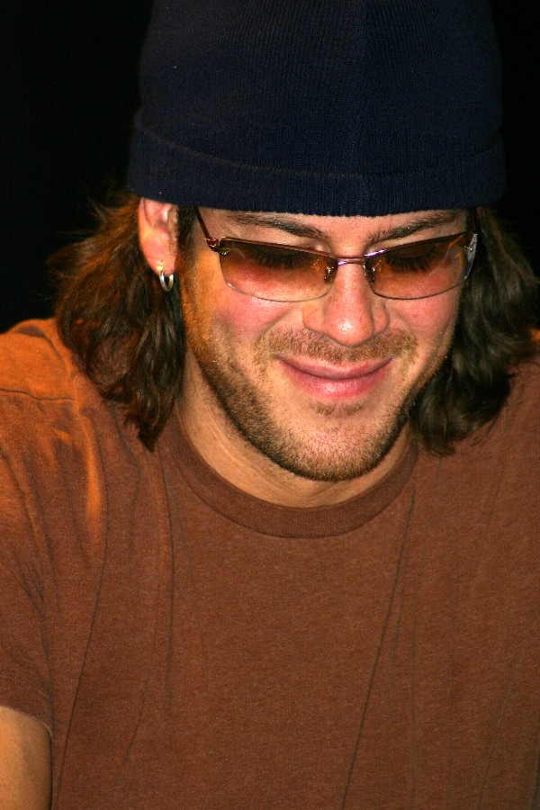 a close up of a man in a hat and glasses holding a cellular phone