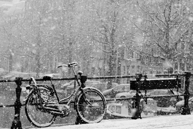 black and white pograph of bicycle on bridge in heavy snow