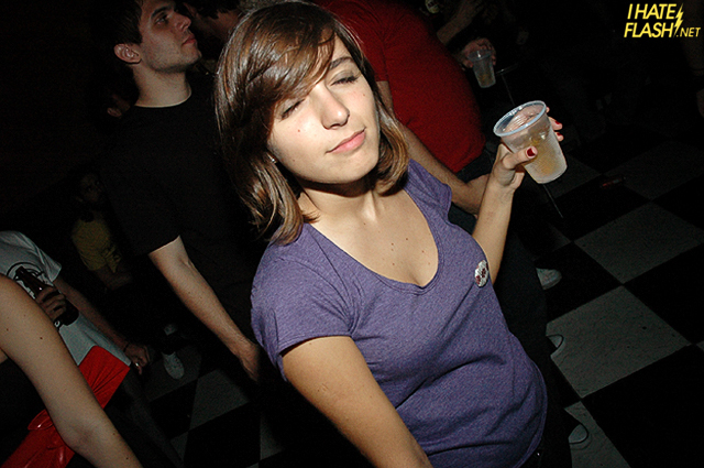 a girl standing in a crowded room holding a drink