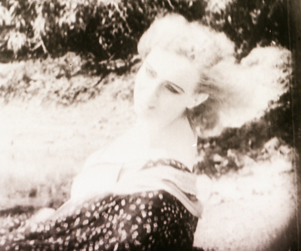 a woman with white hair is sitting by a bush