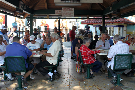 many people are seated at tables together under a shaded gazebo