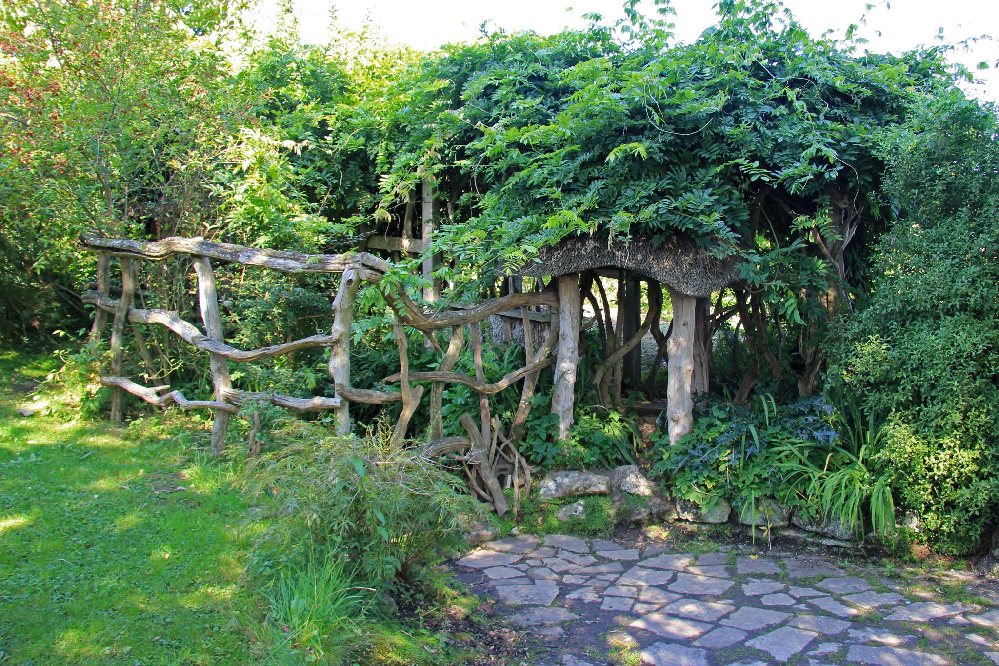 a stone walkway leads to a trellis - like structure with wooden logs sticking out