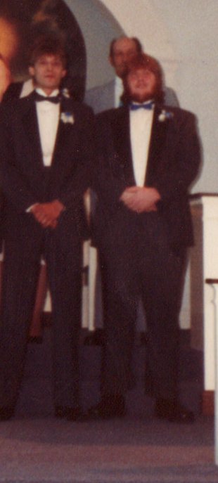 two men wearing tuxedos, stand on stage in front of an audience