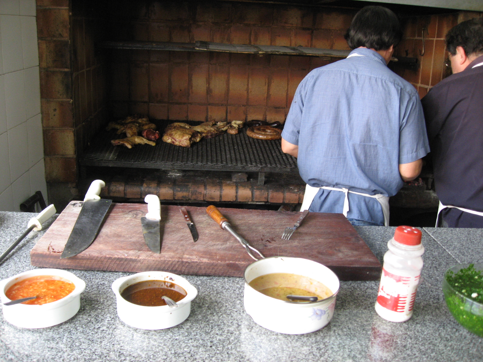 two men with aprons and cooking utensils in front of an oven