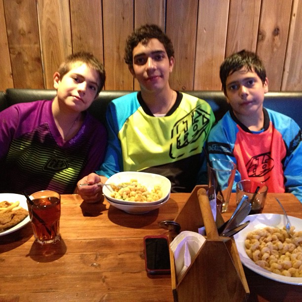 three boys sitting at a table with bowls of food and drink