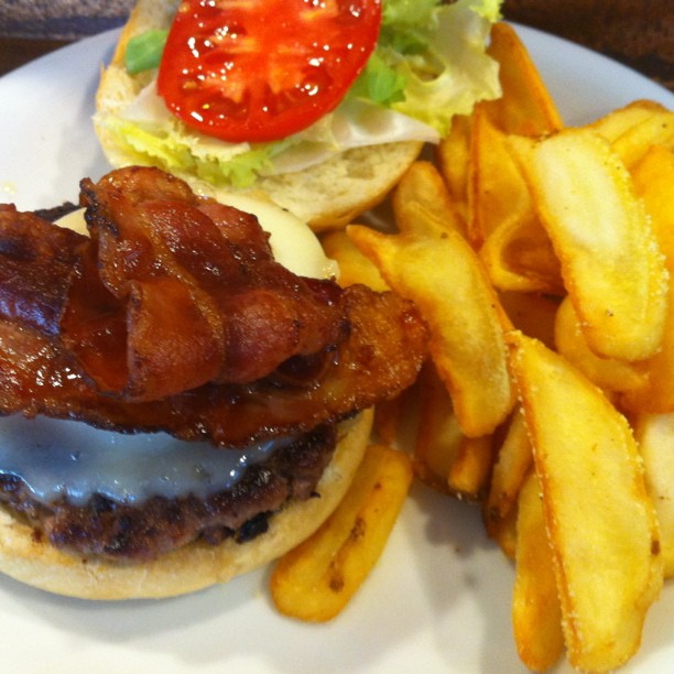 a bacon burger with lettuce, tomatoes and fries on a plate