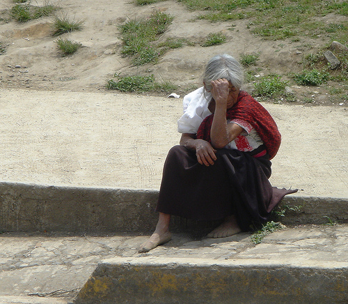 an elderly woman sits on some concrete steps, talking on her phone