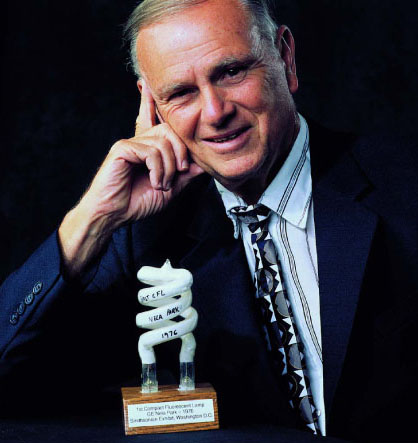 a smiling man with gray hair and a suit holding his finger on a sculpture