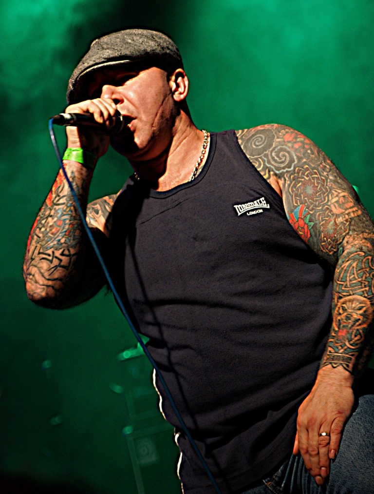 tattooed man singing with his hands on his hips