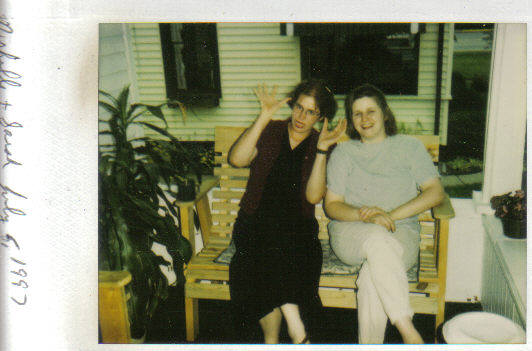 two girls sitting on wooden chairs talking while one woman waves