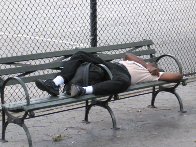 a man sleeping on a bench in front of a fence