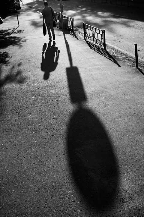 a man walks down a sidewalk as the shadows cast