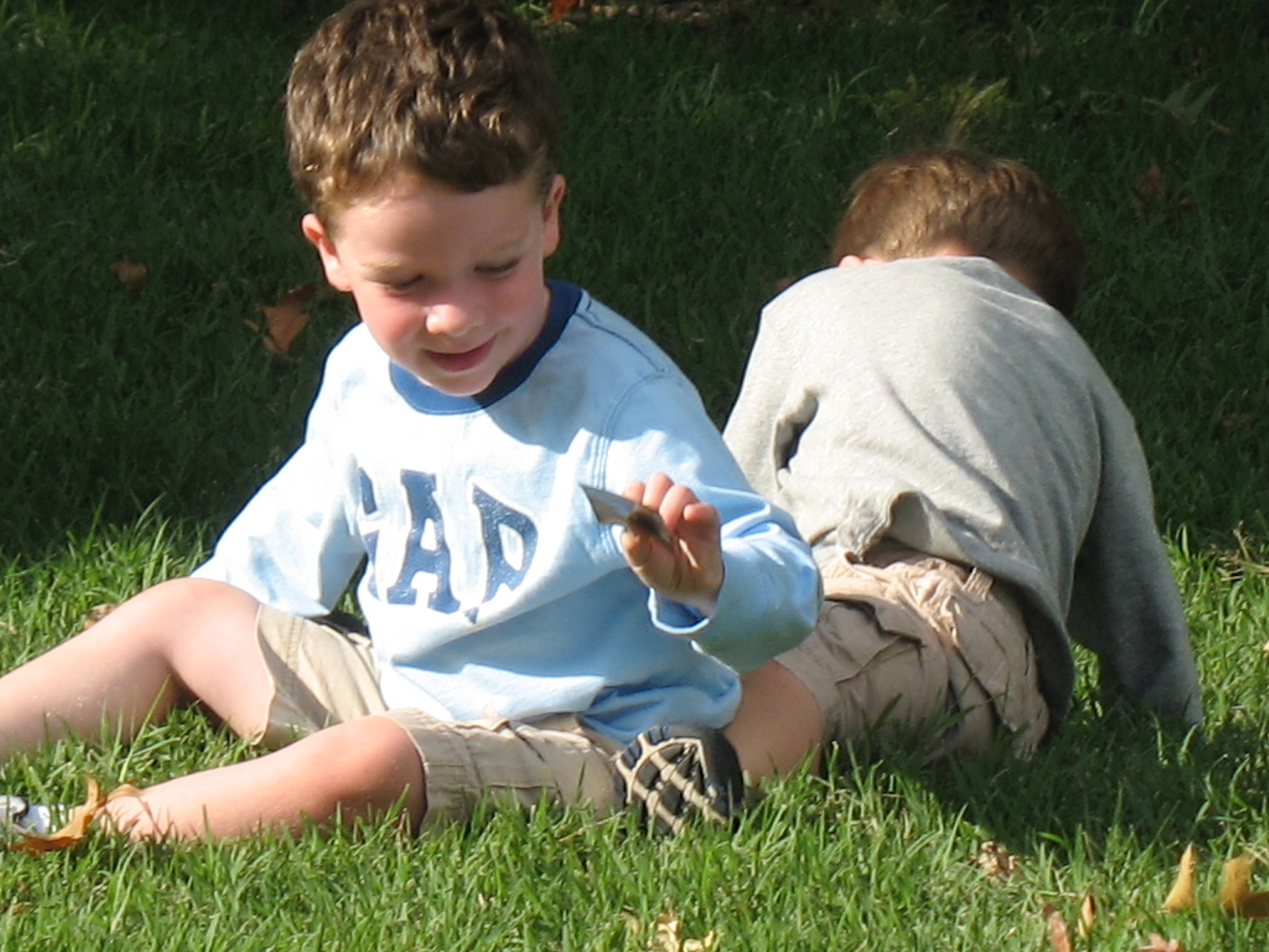 two boys sitting in the grass one looking at his phone
