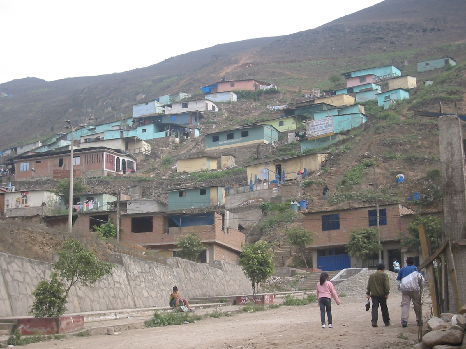 several people walk up a steep hillside as they pass a building
