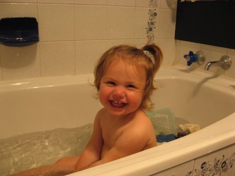 a smiling toddler sitting in the water in a bathtub