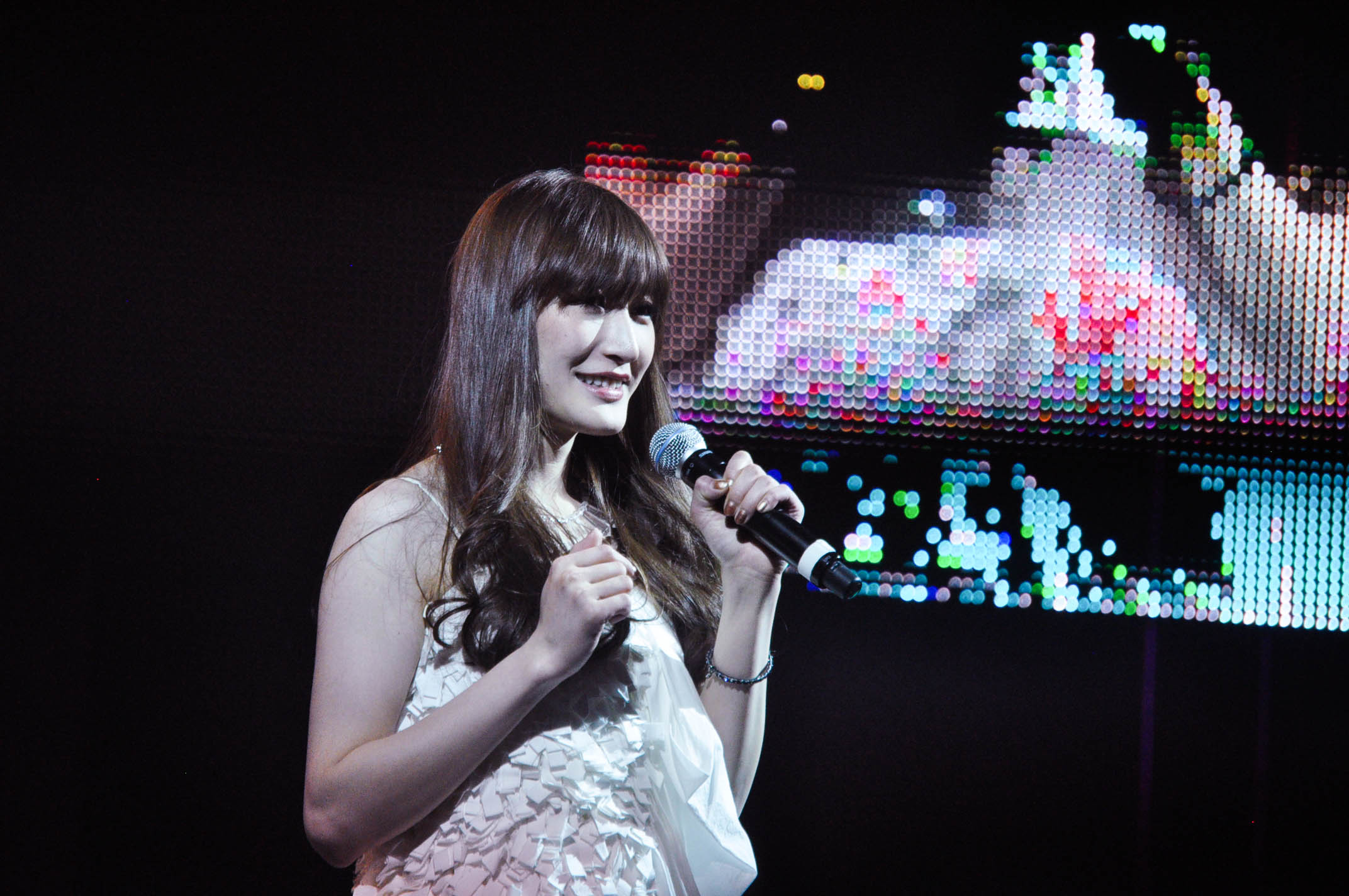 a woman wearing a white dress and microphone in front of colorful background