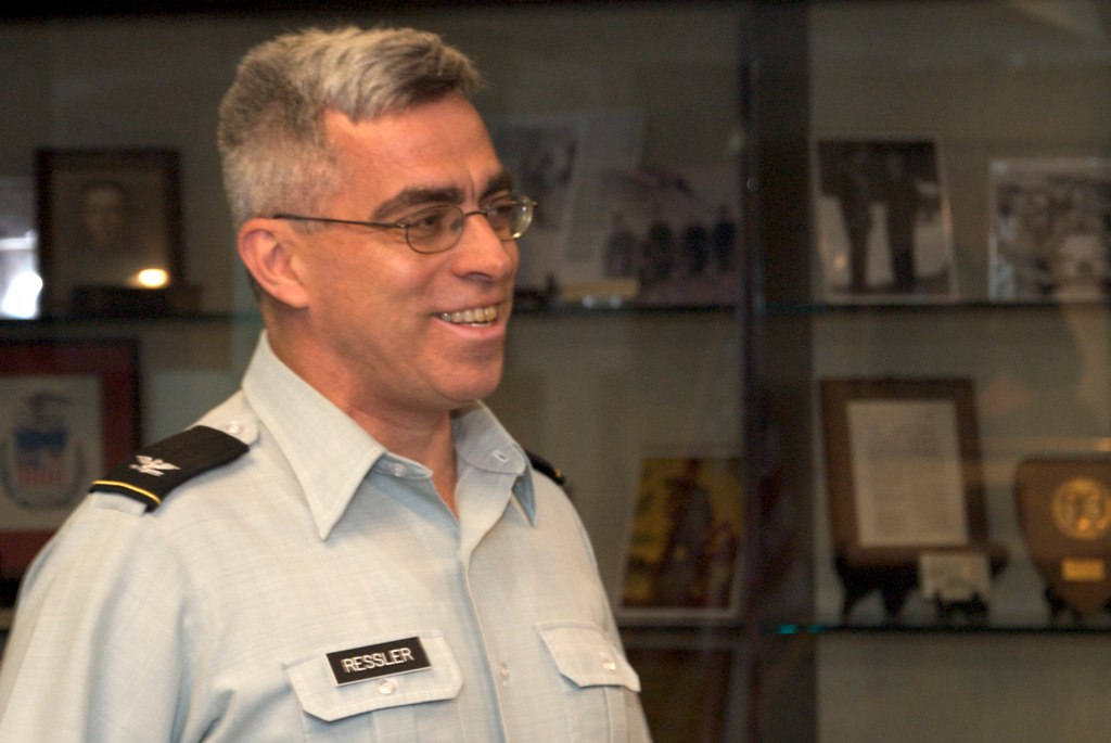 a man wearing glasses and a uniform standing next to shelves with framed pos