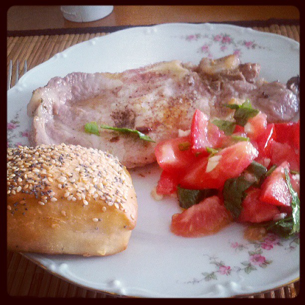 a meat with tomato, onion and sesame seed bread with sprouts on the side