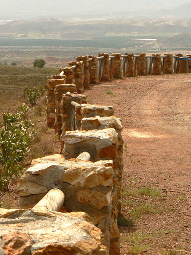 stone fences are on a gravel road with scrub trees