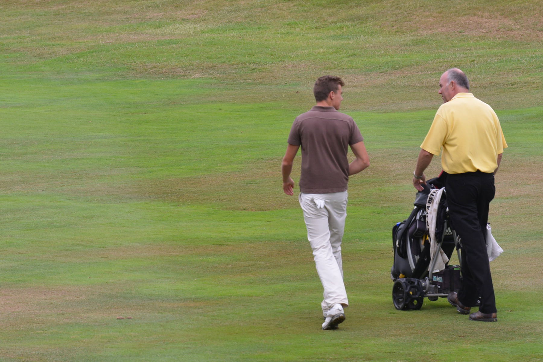 two men walking across a green grass covered field