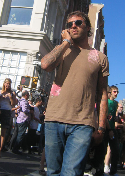 a man with tattoos and sunglasses talks on his cell phone while walking down the street
