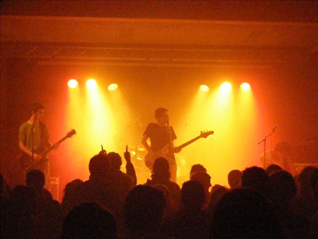 two men playing instruments on stage with lights from the stage behind them