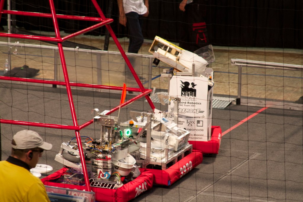 a lego structure sits in the middle of a concrete area with a man behind it