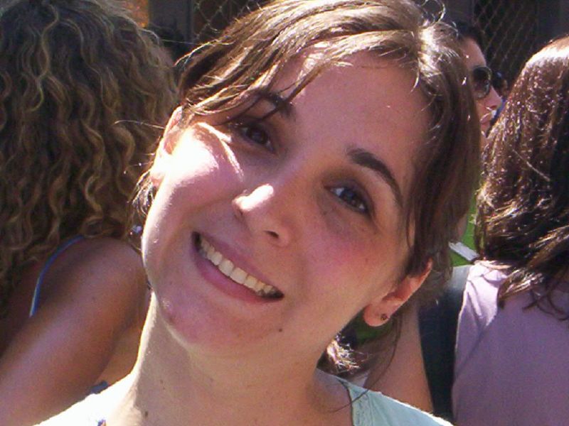 a smiling woman is in front of a chain linked fence