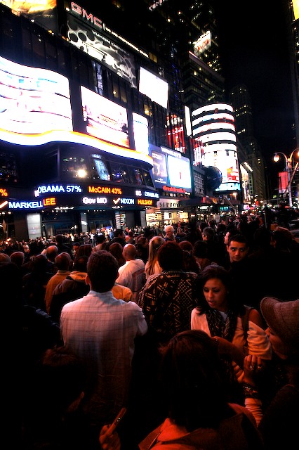 a crowd of people walk down a crowded sidewalk